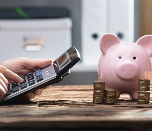 Close up of someone using a calculator next to coin stacks and a piggy bank