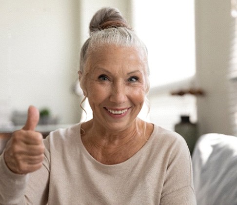 Older woman giving a thumbs-up with her dentures
